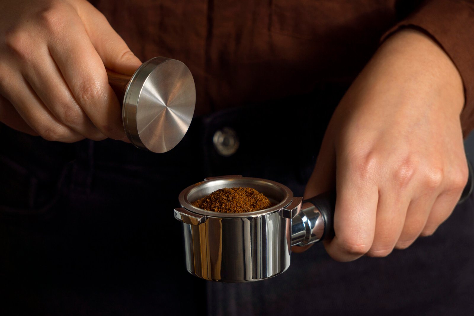 Bir baristanın hassas bir şekilde öğütülmüş espresso kahve çekirdeklerini portafiltreye doldururken gösteren yakın çekim.